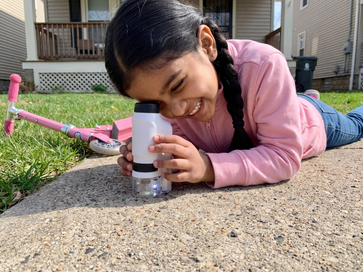 A girl lying on the sidewalk, looking at it through her Miniscope