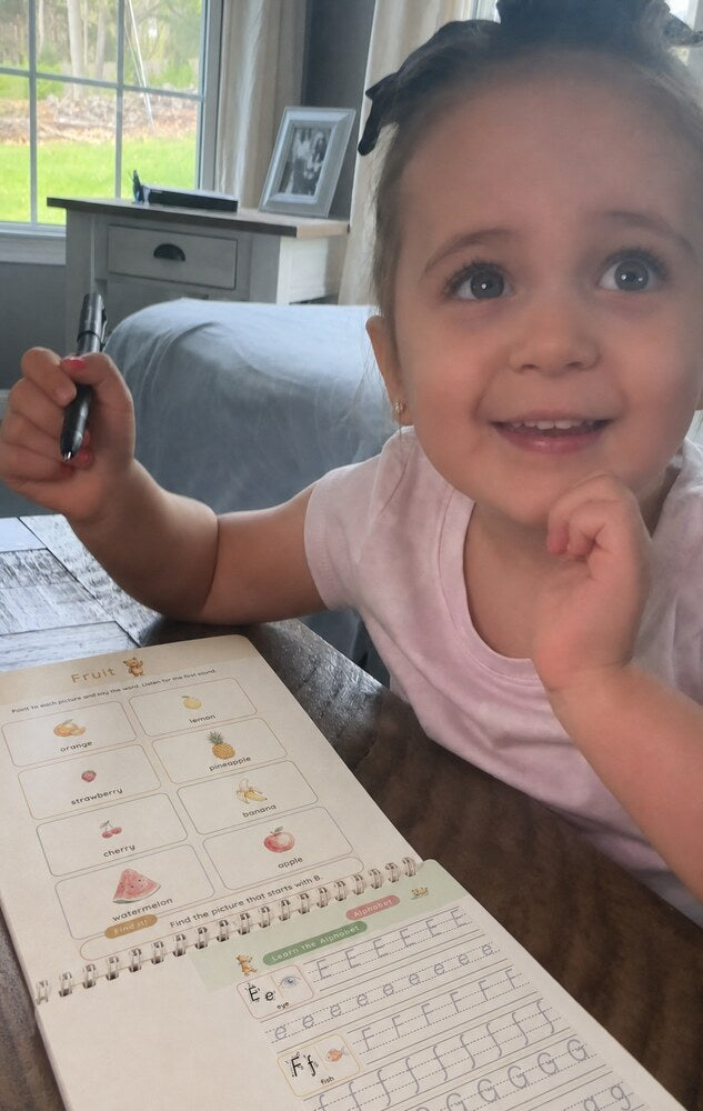 A smiling toddler holds the magic pen over an open copybook