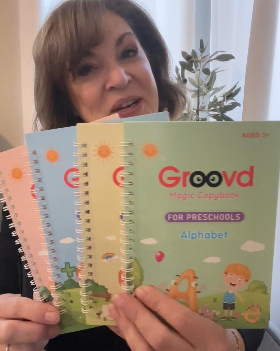 A woman holds up four Groovd copybooks with the Alphabet book in front