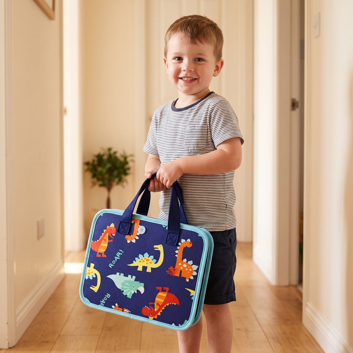 A smiling child carries the closed board by its handles like a small case, its cover printed with cartoon dinosaurs