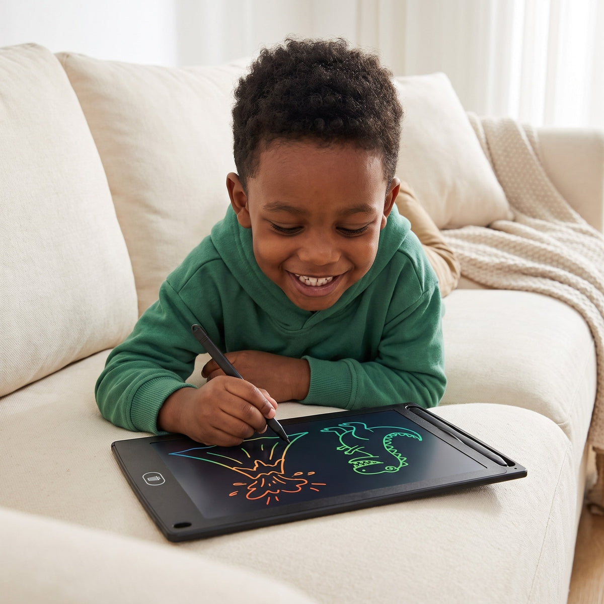 A smiling child lies on a sofa drawing a volcano and a green dinosaur on the tablet with its pen