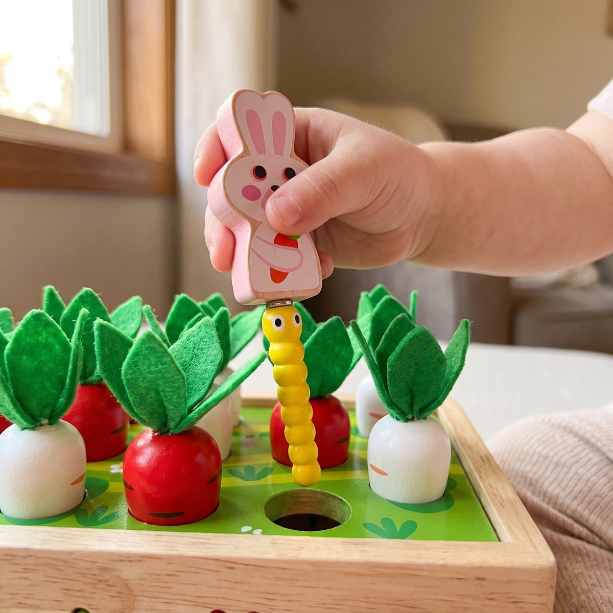 A child's hand holds the wooden rabbit, which picks up a yellow worm with the magnet on its base