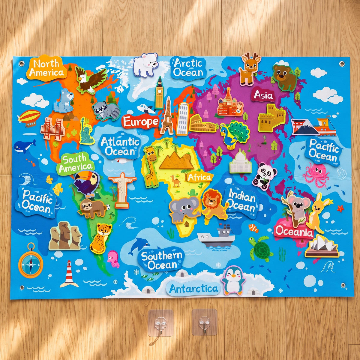 Top view of the whole felt map on a wooden floor with the animal and landmark pieces in place, plus two clear wall hooks