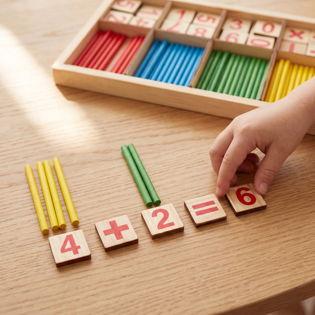 A child's hand places the 6 tile to finish 4 plus 2 equals 6, with yellow and green counting sticks above the numbers.