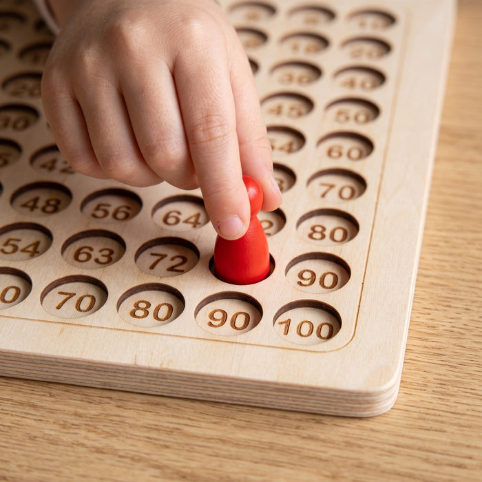 A child's hand puts a red pawn into one of the numbered holes on the wooden board.