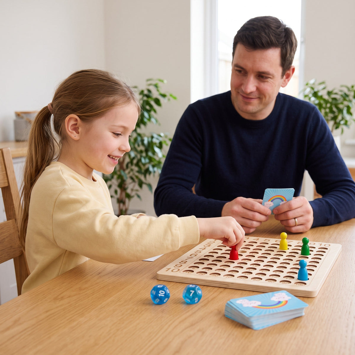 A child and a parent play at a table, the child moving a red pawn on the board while the parent holds a rainbow card.