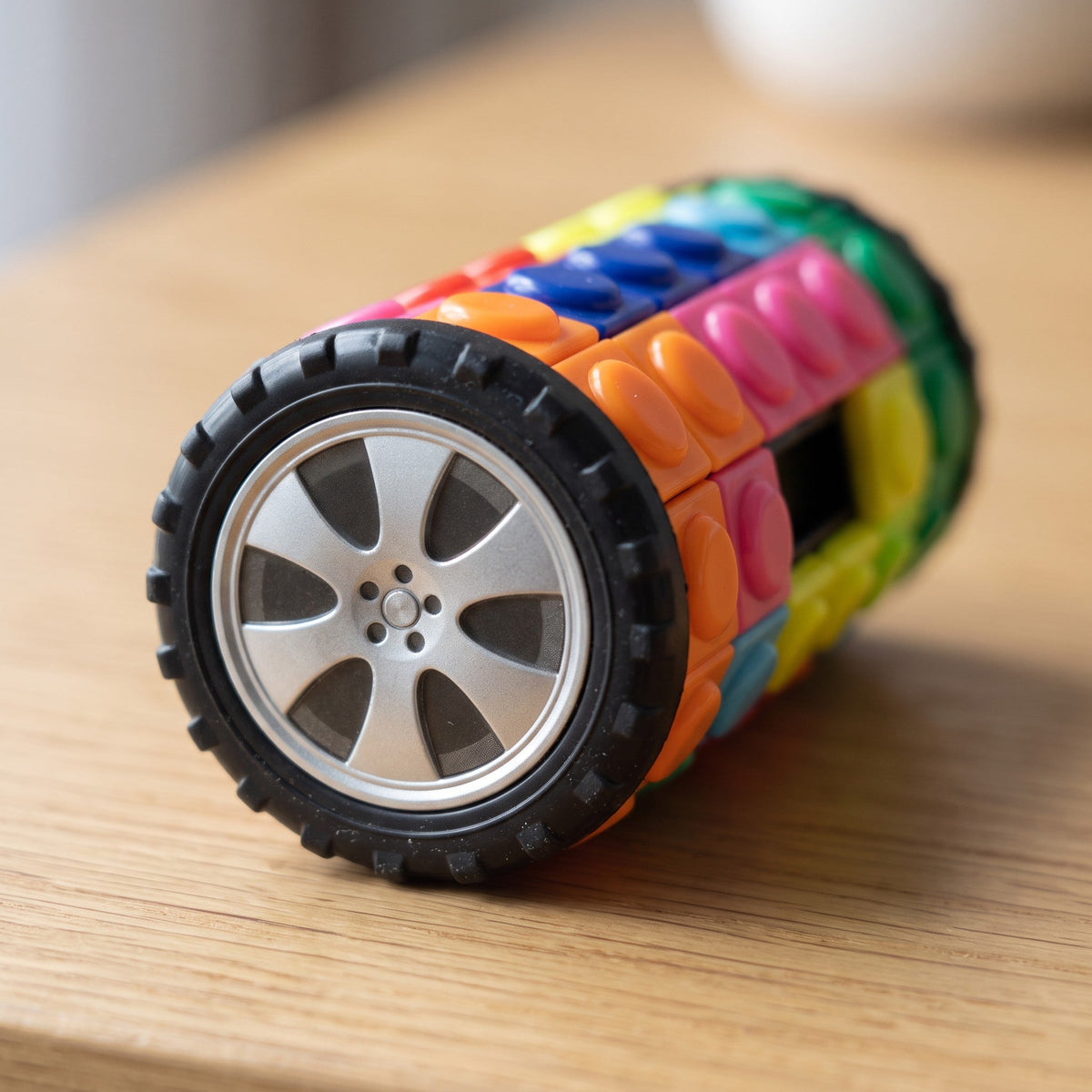 Close-up of a puzzle lying on its side, showing the black toy tire and silver wheel on its end and mixed-up color tiles