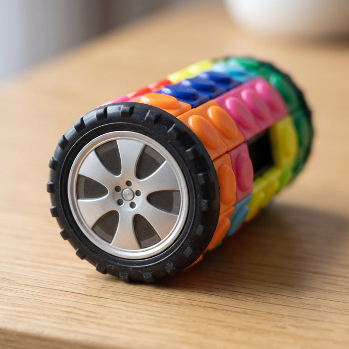 Close-up of a puzzle lying on its side, showing the black toy tire and silver wheel on its end and mixed-up color tiles