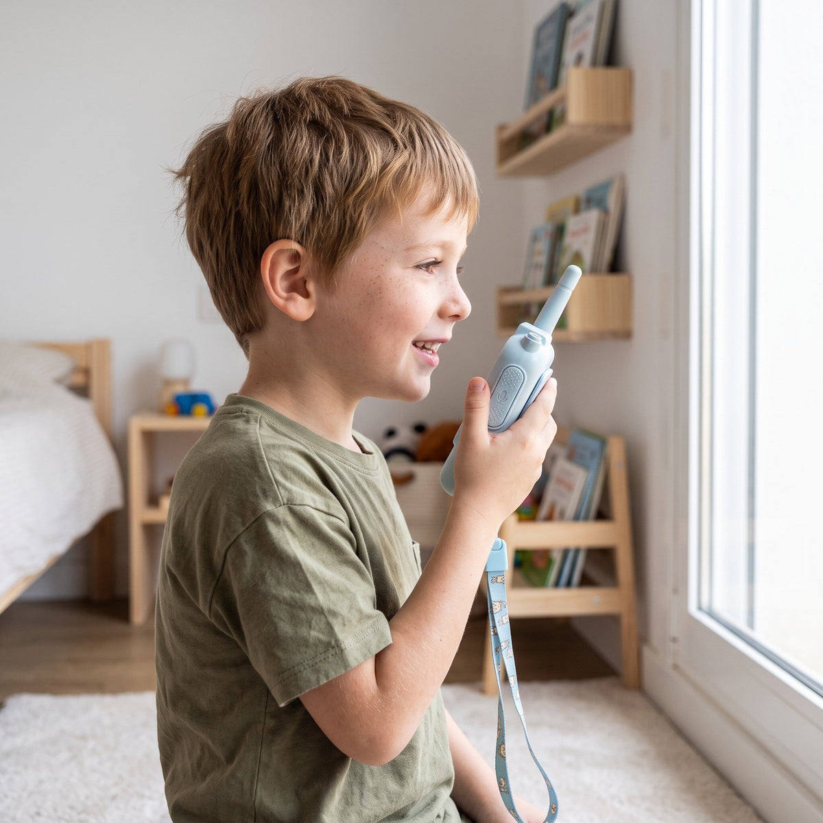 A smiling child holds the pale blue walkie-talkie up and talks into it, with its lanyard hanging down