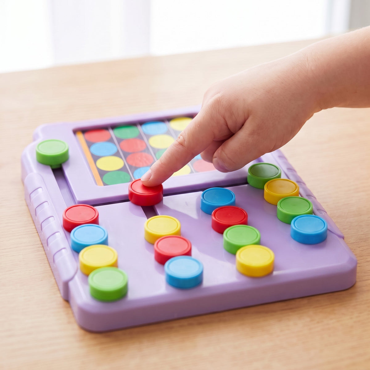 A child's finger pushes a red disc on the purple board, with a pattern card showing in the top window.