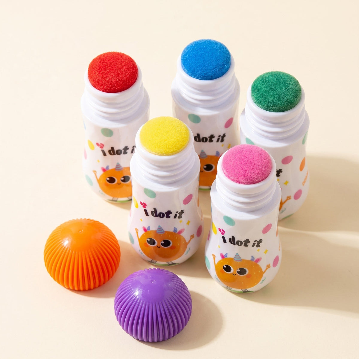 Close-up of five uncapped dot markers showing their round sponge tips in red, blue, green, yellow and pink, with two caps