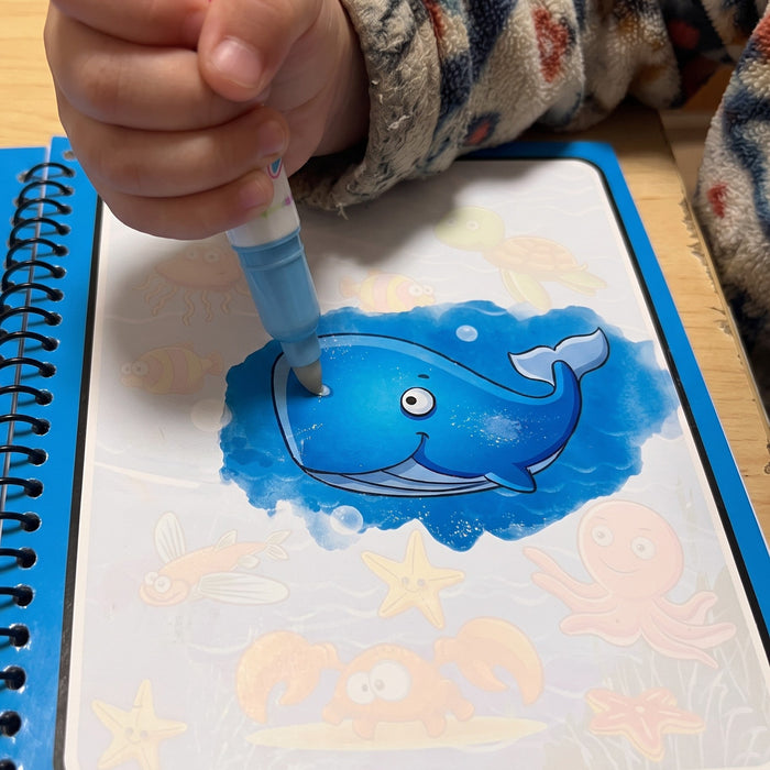 A child runs a water pen over a pale page, and a bright blue whale shows where it is wet, with faint sea animals around it